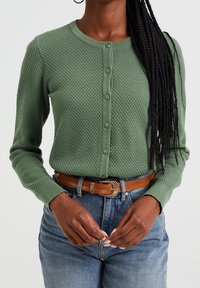Green textured cardigan with a round neckline, front button closure, and long sleeves, paired with high-waisted denim and a brown belt.