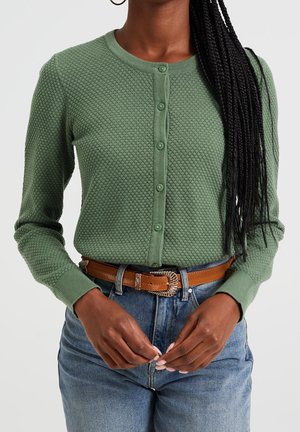 Groene textuur gebreide cardigan met een ronde halslijn, sluiting met knopen aan de voorkant en lange mouwen, gecombineerd met high-waisted denim en een bruine riem.
