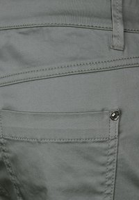 Grå tygbyxor med en slät textur, försedd med bakfickor, synlig sömnad och en knappdetalj på fickan.