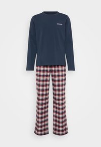 Camiseta de manga larga azul marino con el logo "GUESS", combinada con pantalones de pijama a cuadros en rojo, blanco y azul. Tejido suave, ajuste relajado, piernas rectas.