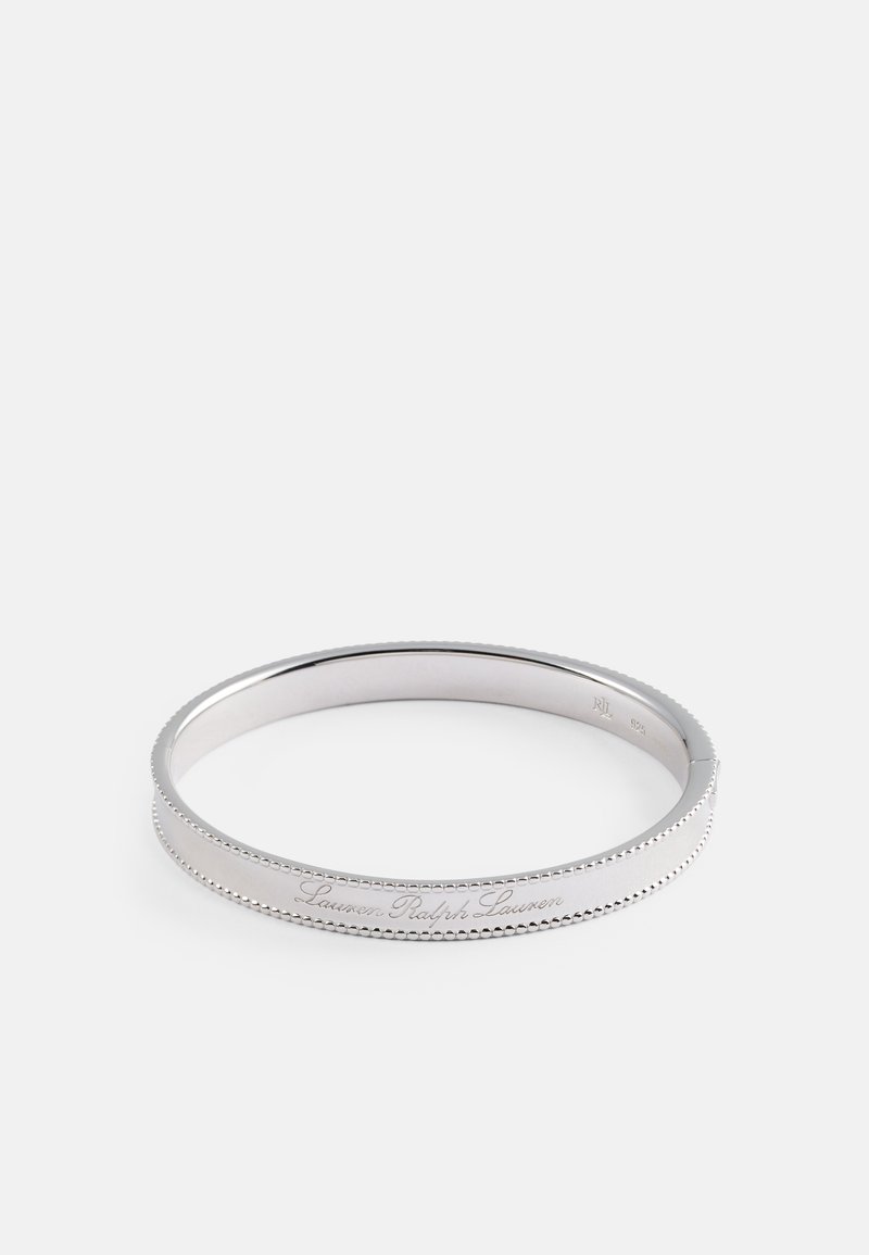 Pulsera de bangle de metal plateado con una superficie lisa y pulida y un logotipo en relieve, con un acento de cuentas a lo largo de los bordes.