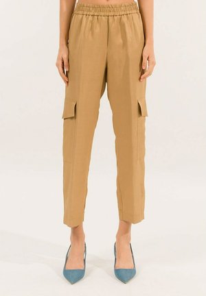 Pantaloni cargo beige con vita elastica, tasche laterali e caviglie affusolate. Il tessuto sembra leggero e liscio.