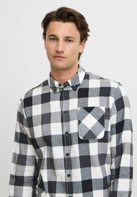 Zwart-wit geruite button-up shirt met lange mouwen, voorzien van een borstzak en een gestructureerde stof.