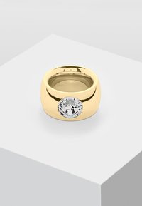 Goldring mit einem großen klaren runden Edelstein in der Mitte, mit einer glatten, glänzenden Oberfläche. Minimalistisches Design, markante Form.