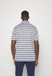Pruhovaný polo tričko v námorníckej modrej a bielej farbe, s krátkymi rukávmi, golierom a textúrovanou tkaninou. Viditeľný zadný šev a zaoblený lem.