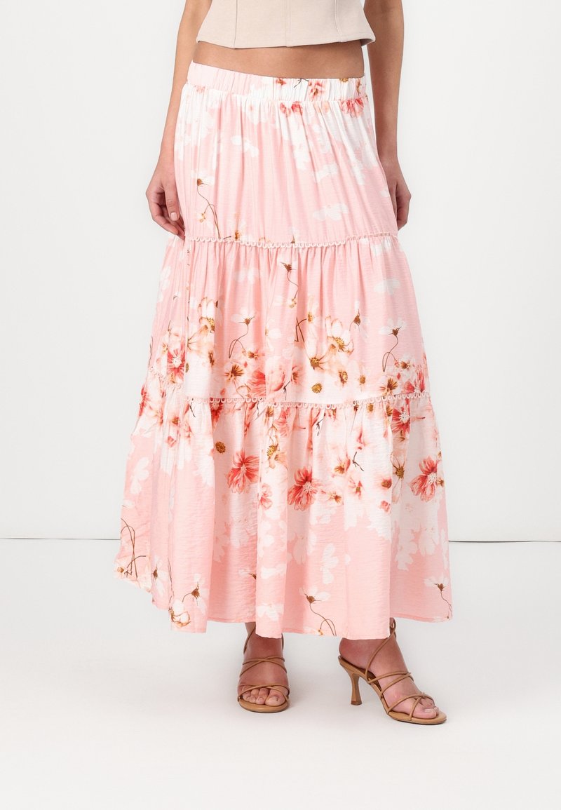 Jupe midi fluide à volants fleurie rose clair portée avec des sandales à talons hauts couleur sable à brides et un top court beige.