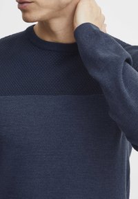 Marineblå strikkegenser med teksturert mønster på øverste del, glatt tekstur på nederste del, samt ribbestrikket rund hals og cuffs.