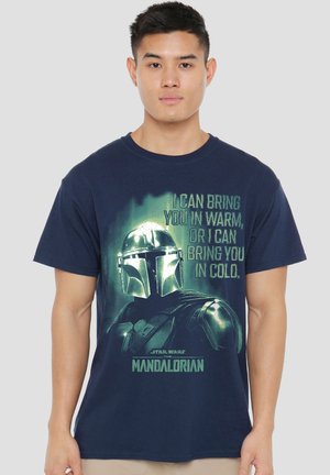 Young man wearing navy blue t-shirt with The Mandalorian helmet and text: "I can bring you in warm, or I can bring you in cold."