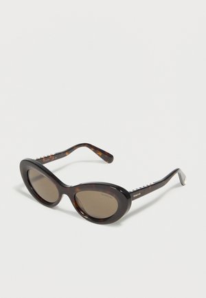 Kassisilmade kilpkonnamustriga päikeseprillid tumedate läätsedega ja Swarovski brändingu kõrval, eksponeeritud valgel pinnal.