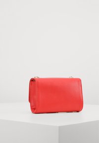 Clutch de cuero rojo con un acabado texturizado, forma rectangular y tapa plegable. Cuenta con una correa de cadena dorada y un diseño minimalista.