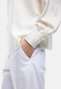 Weiße Satinbluse mit ger gathered cuffs, kombiniert mit glatten weißen Hosen. Die Bluse hat eine lässige Passform und einen abgerundeten Saum.