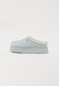 Lichtblauwe instapslippers met een dikke zool, witte gestikte rand en UGG-logo aan de zijkant, weergegeven op een effen witte achtergrond.
