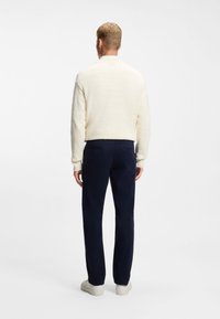 Svetlo krem pulover z teksturo v kombinaciji z mornarsko modrimi hlačami in belimi supergami. Pogled od zadaj, ki prikazuje kontrast barv oblačila.