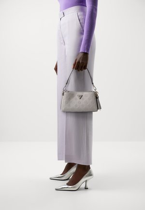 Personne portant un haut à manches longues lavande et un pantalon, tenant un petit sac à main blanc de créateur, et portant des chaussures à talons hauts métalliques argentées.