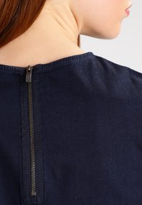 Námořnické modré tričko s kulatým výstřihem a krátkými rukávy, s kovovým zipem na zadní straně a hladkým povrchem textilu.