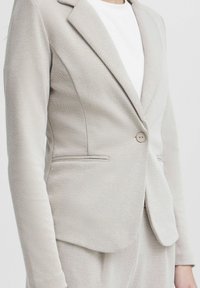 Ljus beige blazer med en texturerad yta, enkel knäppning och två sidofickor. Har en skräddarsydd passform och vassa slag.