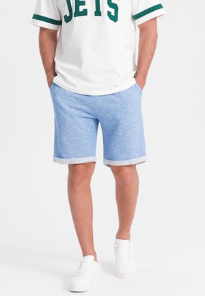 Shorts en mélange de coton bleu clair avec une texture chinée et des ourlets roulés, associés à un t-shirt blanc avec une inscription verte.