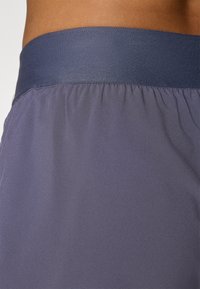 Navyblauwe tailleband met een gladde textuur; gecombineerd met een lichtpaarse stof in een zachte, rekbare structuur voor comfort.