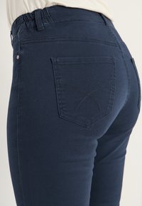 Mörkblå stretchjeans med elastisk midja, har en bakficka med kilsydd detalj och en smal passform.