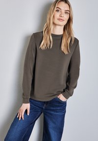 Felpa verde oliva in un materiale morbido, con maniche lunghe e scollatura rotonda, abbinata a jeans a gamba larga in denim blu.