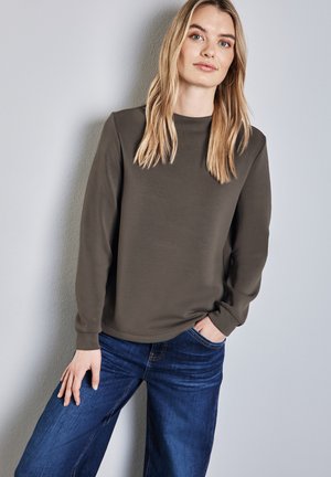 Olivenfarbener Pullover aus weichem Material mit langen Ärmeln und Rundhalsausschnitt, kombiniert mit blauen Jeans im weiten Schnitt.