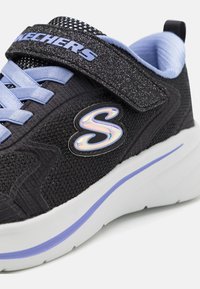 Sneaker en mesh noir avec des lacets bleus et une sangle scintillante. Présente un logo irisé et une semelle blanche avec une ligne d'accent en lavande.