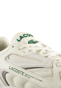 Sneaker Lacoste bianca con materiali in mesh e pelle, logo verde, design con lacci e dettagli testurizzati sui lati e sulla punta.