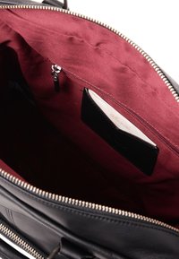 Interno di una borsa a tracolla in pelle nera con un rivestimento in tessuto bordeaux, una tasca con cerniera e un vano per carte con un inserto di carta.