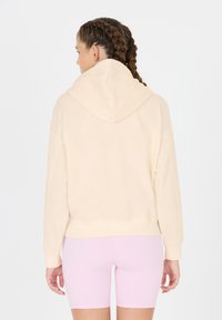 Hoodie aus weichem beigem Stoff, mit lockerem Schnitt, gerippten Bündchen und verkürztem Saum, kombiniert mit rosafarbenen Radshorts.