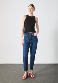 Zwarte geribbelde tanktop gecombineerd met hooggepaste blauwe jeans en rode haksandalen. Soepele textuur en gesloten ontwerp.