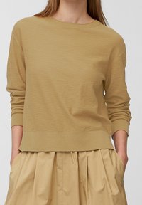 Maglione in maglia color kaki con scollatura tonda e polsini a coste. Texture morbida, vestibilità comoda e design leggermente corto. Abbinato a una gonna chiara.