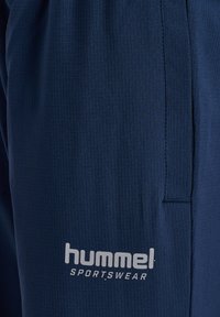 Navy sportbyxor med ribbad textur, med en vit "hummel"-logotyp och en sydd fickdetalj på sidan.