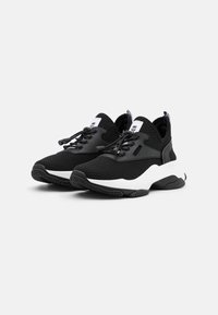 Schwarze Sportschuhe mit einem strukturierten Strickobermaterial, kontrastierender weißer Sohle und schwarzen Akzenten. Verfügt über verstellbare Schnürsenkel und eine Zuglasche.