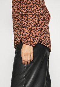 Blus med lång ärm i ett rosa och svart blommönster, puffiga ärmar och elastiska ärmslut, kombinerad med svarta byxor i faux läder.