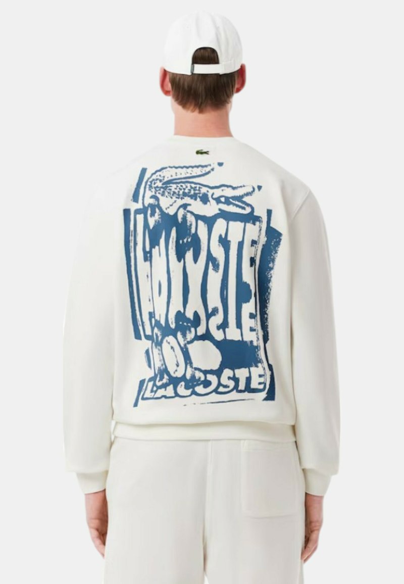 Sudadera blanca con un gran estampado gráfico azul de un cocodrilo y texto en la parte de atrás. Material suave con puños y dobladillo de canalé.