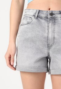 Šedé džínsové šortky s ohrnutým lemem, vybavené předními kapsami, zapínáním na knoflík a vybledlým efektem s viditelnými švy.