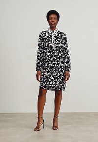 Black and white collared dress featuring an animal print, long sleeves, and a relaxed fit, paired with strappy black heels.