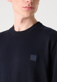 Námořnický pletený svetr s kulatým výstřihem, na hrudi s malým texturovaným čtvercovým logem. Měkká, hladká textura a přiléhavý střih.