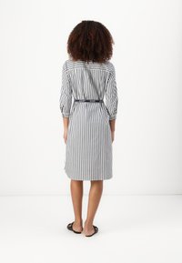 Pruhované šaty košilového střihu v námořnické modré a bílé barvě, s páskem v oblasti pasu a rukávy do tří čtvrtin. Hladká tkanina a délka do kolen.