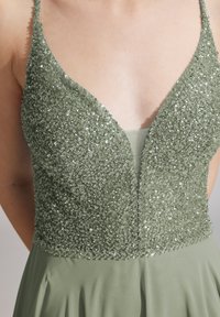 Grünes Paillettenkleid mit tiefem V-Ausschnitt, das einen figurbetonten Oberteil mit verziertem Stoff und einen fließenden Rock hat.