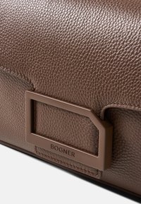 Brun lædertaske med en tekstureret overflade, et rektangulært brunt metalbeslag og et præget "BOGNER" logo.