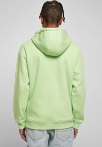 Lysegrønn hettegenser med stor hette, ribbet mansjetter og myk tekstur. Brukt sammen med lyseblå jeans med en avslappet passform.