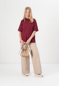 Burgunderfarget oversized t-skjorte, beige vide bukser og en flerfarget håndveske. Håndvesken har et plisse-design og et flettet håndtak.