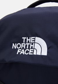 Zaino in tessuto blu navy con logo bianco ricamato di The North Face, caratterizzato da una texture liscia e una moderata lucentezza.
