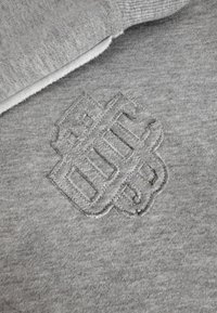 Grijze stof met een verhoogd, gestikt geometrisch patroon met elkaar overlappende vormen en lijnen nabij de gevouwen rand.