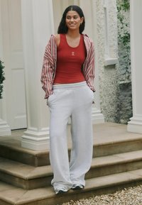 Canotta rossa leggera con testo bianco, abbinata a pantaloni della tuta grigi oversize e una giacca a righe. Design casual con vestibilità comoda.