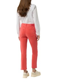 Coral-colored, fitted pants with a mid-rise waist, featuring four pockets and a tag on the back. Paired with beige shoes.