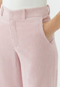 Pantalon en velours côtelé rose clair à rayures verticales, avec poches latérales et texture douce, partiellement visible à la taille.