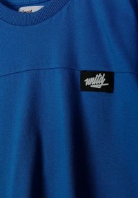 Sweat-shirt bleu à col rond avec un patch rectangulaire noir affichant le texte stylisé blanc "unity" sur la poitrine.