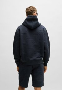 Navy blue hoodie with a hexagonal pattern, featuring a hood and ribbed cuffs. Paired with matching shorts, both crafted from soft material.
